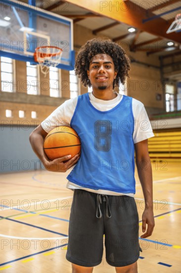 Smiling basketball player holding a ball while standing confidently on the court of an indoor arena, embodying passion and athleticism