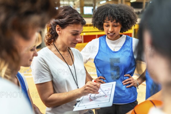 Basketball coach explaining game strategy to her team using whiteboard, during training in the court