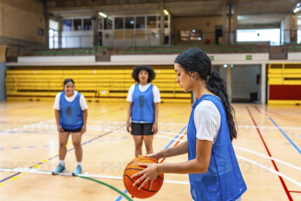Young woman basketball player holding a ball while practicing with her team on the court in a gym, focusing on skills and teamwork