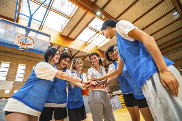 Female basketball players and their coach stacking hands, demonstrating teamwork and unity before a basketball game inside a gymnasium