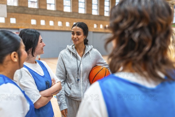 Female basketball coach holding a ball and engaging with her team during an intense training session in the gym, fostering teamwork and motivation