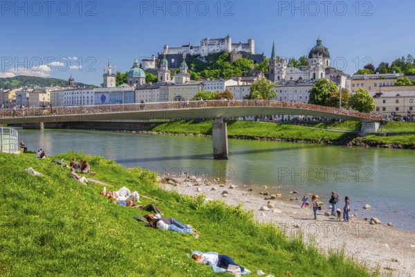 Sunbathers on the banks of the Salzach river next to Hohensalzburg Fortress, Salzburg, Salzach Valley, Salzburg Province, Austria