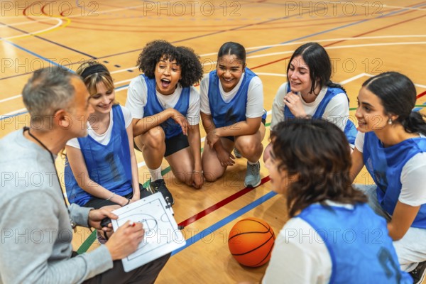 Female basketball team listening to their coach explaining game strategy on a clipboard during a time out