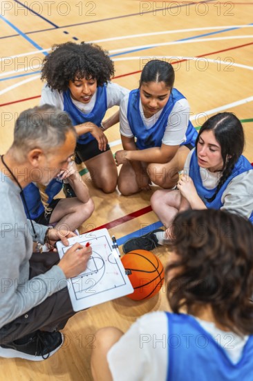 Basketball coach explaining game strategy to female athletes on a clipboard, during a time out in a basketball court