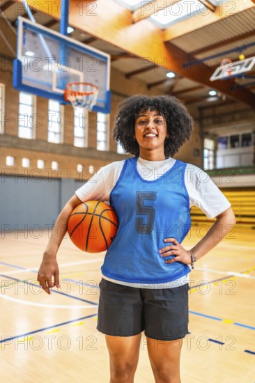 Young woman basketball player smiling while holding a ball on the court, exuding confidence and readiness for training sessions