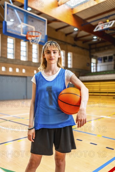 Young female basketball player standing on the court, holding a basketball, ready for the game, showing confidence and determination