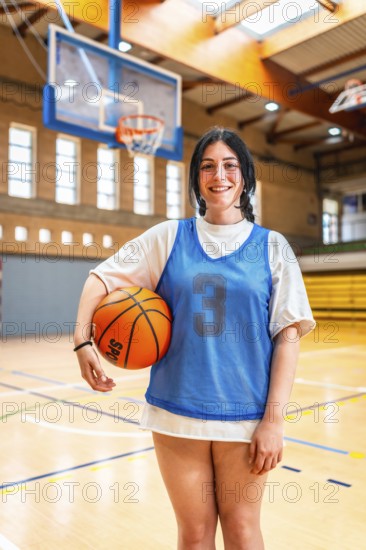 Female athlete smiling and holding basketball in a gymnasium, ready for training or competition