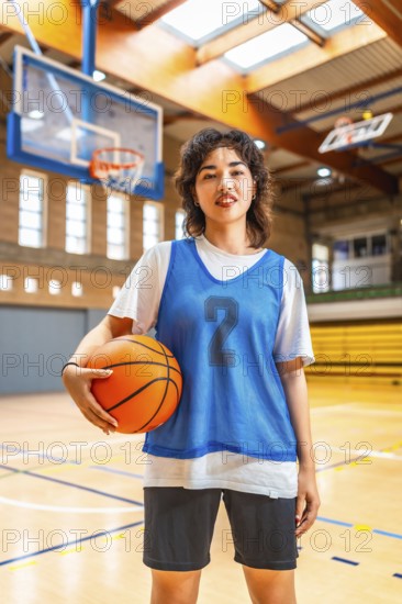 Young asian woman basketball player holding a ball in an indoor court, ready for training or competition