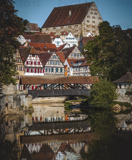Half-timbered houses with red roofs are reflected in the river next to a wooden bridge in a picturesque medieval setting in the town of Schwäbisch Hall, Baden-Württemberg, Germany