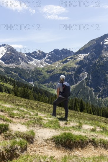 Hikers on a meadow in front of an impressive alpine backdrop in Kleinwalsertal, Austria