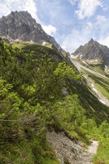 Stony path in an alpine mountain landscape under a blue sky with clouds and a view of the small and large Widderstein mountain peaks in Gemsteltal, Kleinwalsertal, Austria