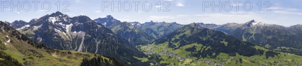 An expansive mountain panorama with green valleys under a partly cloudy sky with a view of the Hohe Ifen in Kleinwalsertal, Austria