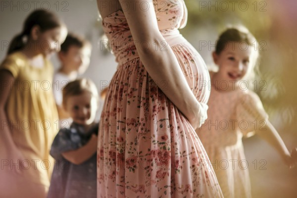 Woman with pregnant belly with happy children in blurry background, AI generated