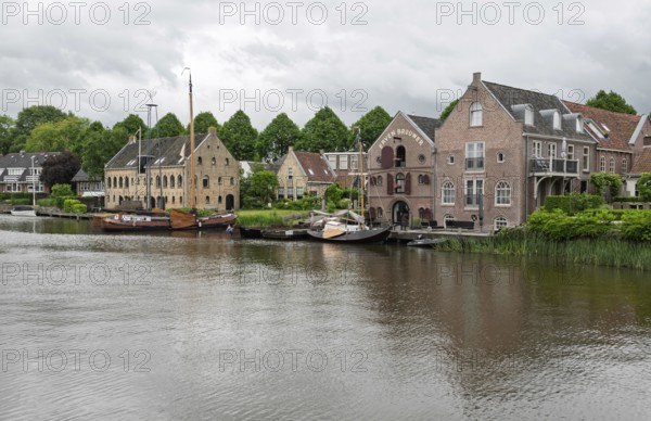Tranquil river landscape with boats and brick buildings under a cloudy sky, Dokkum, Friesland, Netherlands