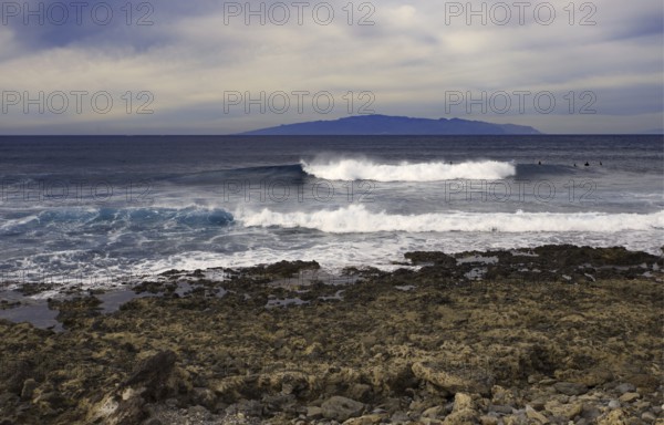 Coast with turbulent waves in front of a distant island (La Gomera) on the horizon, Tenerife, Canary Islands