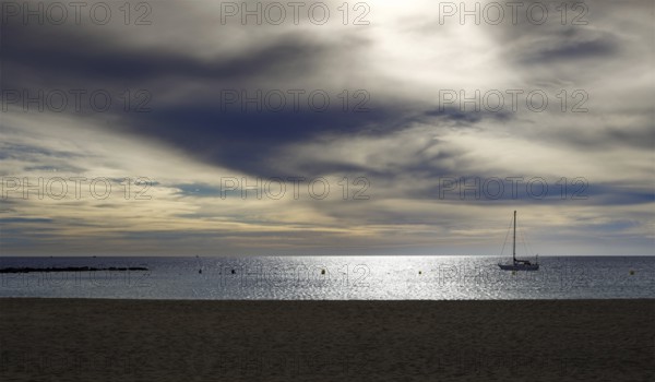 A sailboat anchored in calm waters under a dramatic cloudy sky, Tenerife, Canary Islands