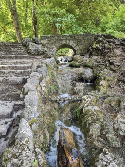A small stone bridge over the Brühlbach, wild and romantic stream and source of the Urach waterfall with natural rock formations in the wooded area, Bad Urach