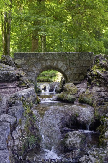 An old, small stone bridge over the Brühlbach, wild and romantic stream and source of the Urach waterfall in a dense forest, Bad Urach