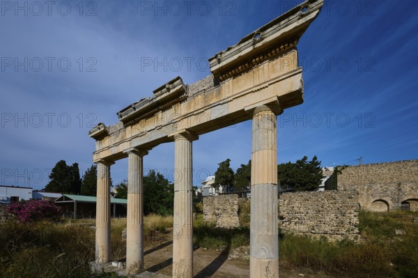 Three ancient columns with a fragment of the entablature, surrounded by ruins and blue sky, Xysto Columned Hall, Gymnasio, Archaeological Site, Western Excavation, Kos Town, Kos, Dodecanese, Greek Islands, Greece
