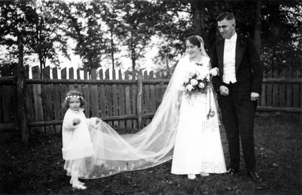 Wedding couple with flower child, bridal couple with little girl in the garden holding the wedding dress, historical photo