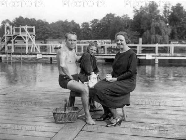 Picnic in outdoor swimming pool, family sitting on a jetty by the lake, relaxing in summertime, historical photo