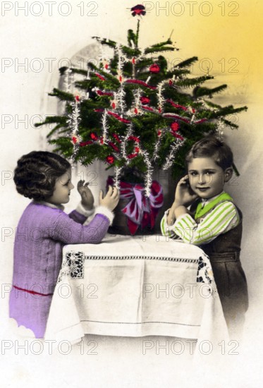 1920, 2 children under a Christmas tree, Two children decorating a small Christmas tree on a table, Historical photo