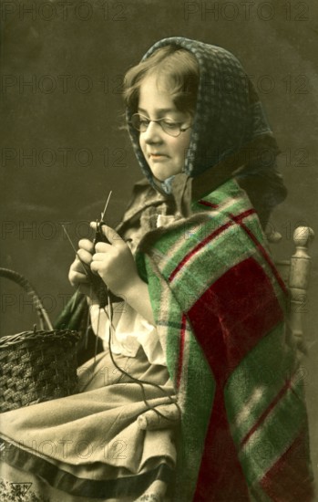 1920 Girl dressed as grandma knitting, girl with knitting needles and glasses in traditional dress knitting, historical photo