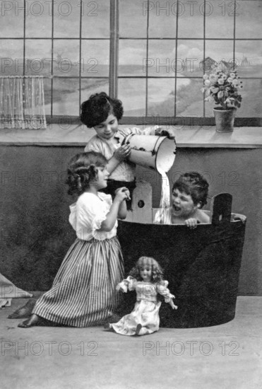 1910 Child being bathed by children, Two children playing in a black bathtub with dolls, Historical photo