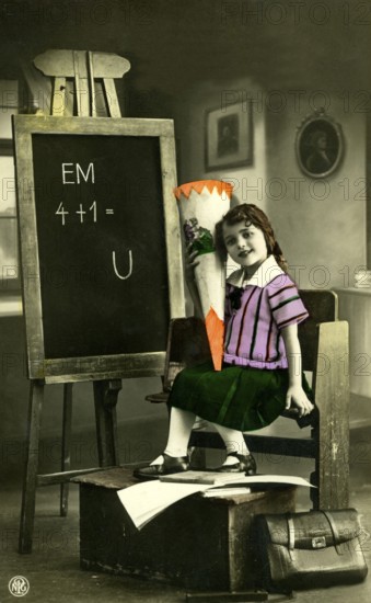 1920 A girl's first day at school, child with a sugar cone in front of a blackboard in a vintage scene, historical photo