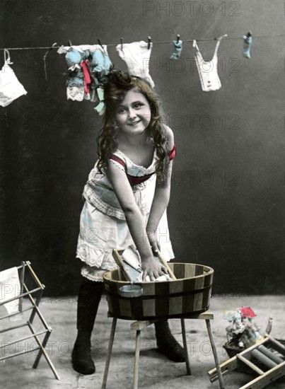 Girl at the washboard, 1920, Girl washing clothes in a wooden bucket, in the background more clothes hanging on a line, historical photo