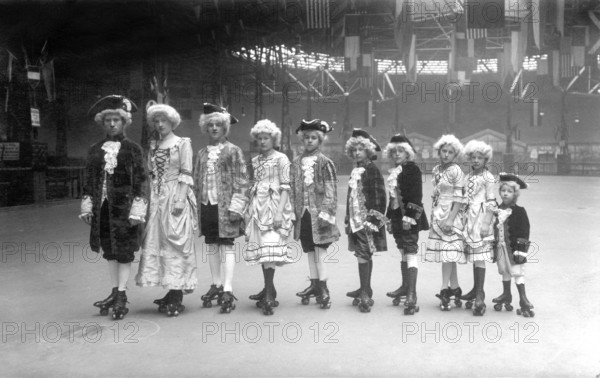 Group in historical costumes on roller skates from big to small, 1920, Group of children in historical costumes on roller skates posing in a large hall with flags on the ceiling, Historical photo