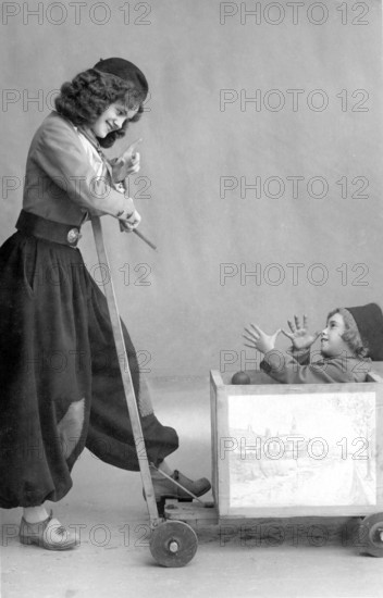 Nanny joking with child in wooden wagon, 1920, Girl pulling a little boy in a wooden toy wagon, both laughing and having fun, historical photo