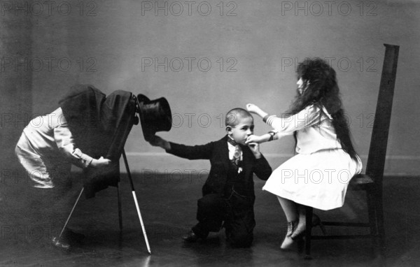 Children photograph hand kiss, 1920, A boy in suit and top hat playing with two other children, one child hanging upside down on a chair, historical photo