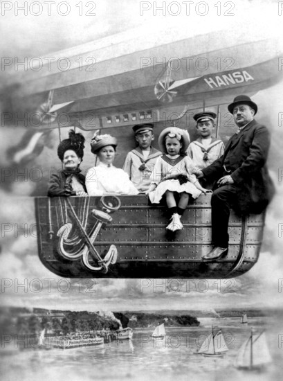 Family in balloon dummy, 1910s, A family sits in the gondola of an airship with the name Hansa over a river, historical photo