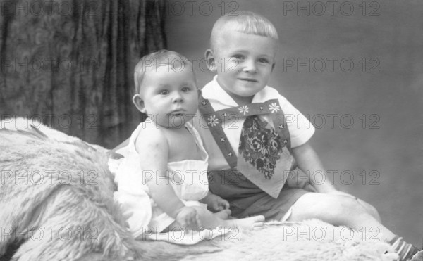Two little boys on bed, 1930s, An older child holding a baby sitting on fur in a studio portrait, Historical photo