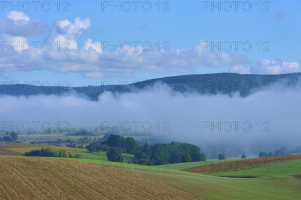 Fog moves through hilly landscape with blue sky, Mönchberg, Miltenberg, Spessart, Bavaria, Germany