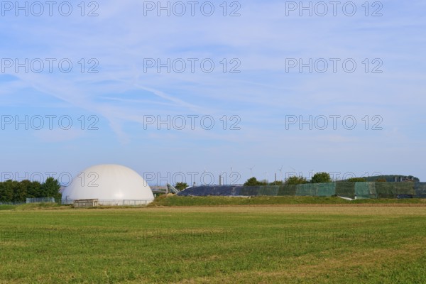 Field with a biogas plant and wind turbines under a blue sky, Germany