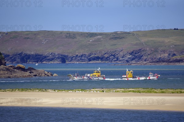 Two small passagi in blue water against a rocky coastline and green cliffs, Camel Trail, Padstow, Cornwall, Cornwall, England, United Kingdom