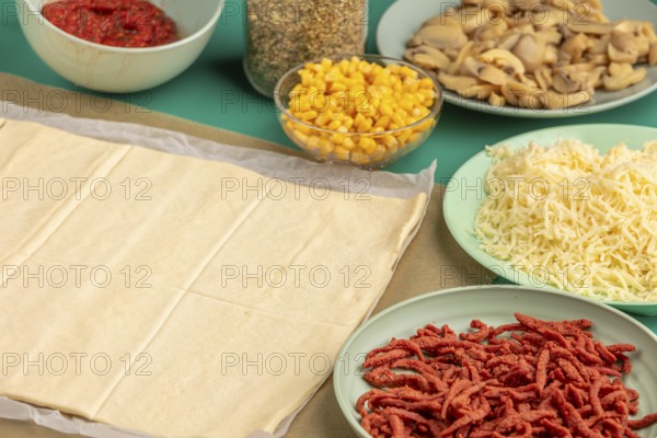 Pizza, dough on baking paper with prepared ingredients in trays