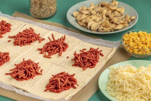 Sliced dough squares with tomato paste and bacon alongside other ingredients for pizza, balls