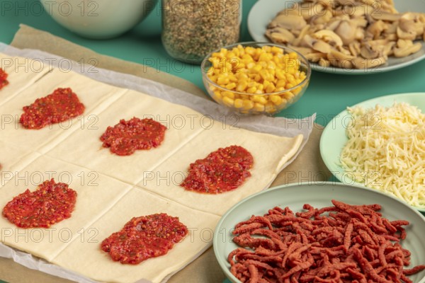 Cut pastry squares with tomato paste and prepared ingredients