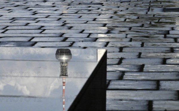The top of the television tower is reflected on a stone pedestal on the north side of the Reichstag building next to a rough pavement on which it had rained lightly a short time in front of