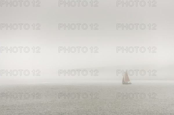 A sailing boat is travelling on the ocean on a cloudy day. The sky is overhanging and the water is calm. Camaret sur mer, Crozon, Finistere, Brittany, France