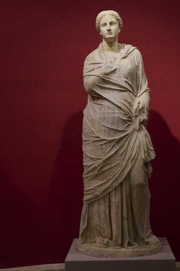 Full-length portrait of an ancient female statue in elaborate drapery against a red background, Archaeological Museum, Kos Town, Kos, Dodecanese, Greek Islands, Greece
