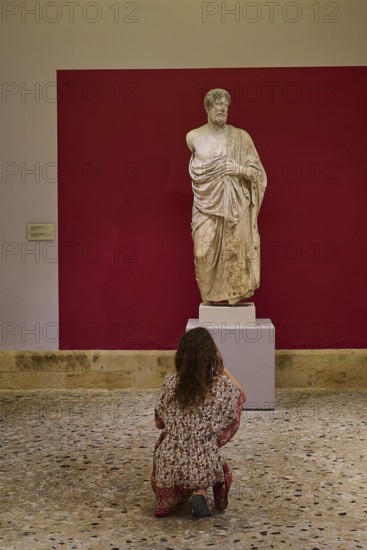 Woman observing an ancient marble statue of a man in a museum, Archaeological Museum, Kos Town, Kos, Dodecanese, Greek Islands, Greece