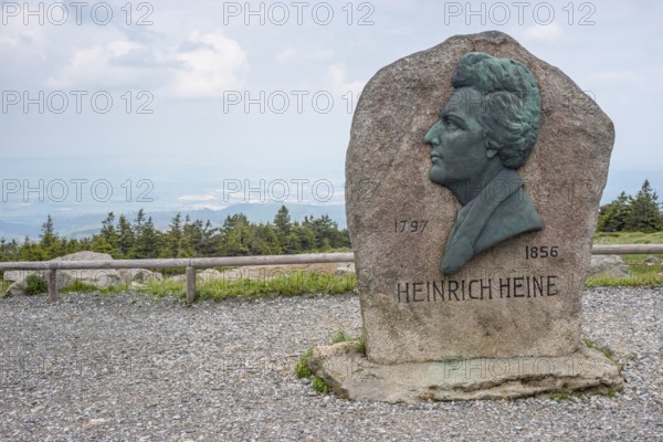 Heinrich Heine memorial, Heine memorial on the summit of the Brocken, summit plateau, granite stone with Heine plaque, portrait of the poet on bronze, inscription, year of birth, year of death, rock, forest of spruces, hazy, veiled view of the north-eastern Harz foreland, view with cloudy sky, Brocken, Harz National Park, Harz, Saxony-Anhalt, Germany