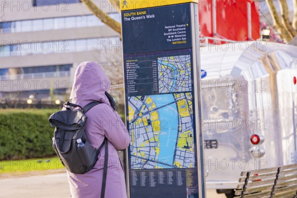 Woman wearing warm clothes looking at a map at a city map kiosk, London, United Kingdom, World