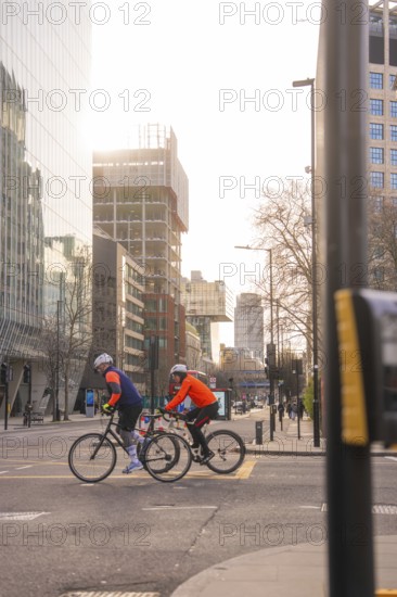 Two cyclists ride on an urban road, sunlight reflected on the buildings, London, United Kingdom, World