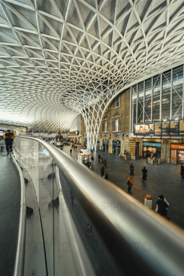 Wide angle view of a busy train station with glass roof and escalators, King's Cross Station, London, United Kingdom, World