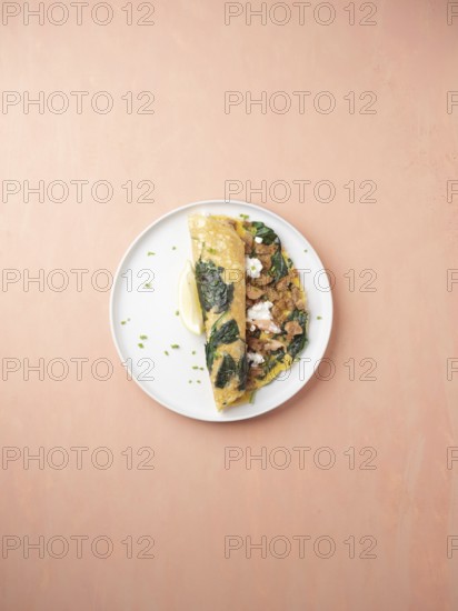 Savory omelet with spinach, crumbled sausage, and lemon wedge on a plate for breakfast